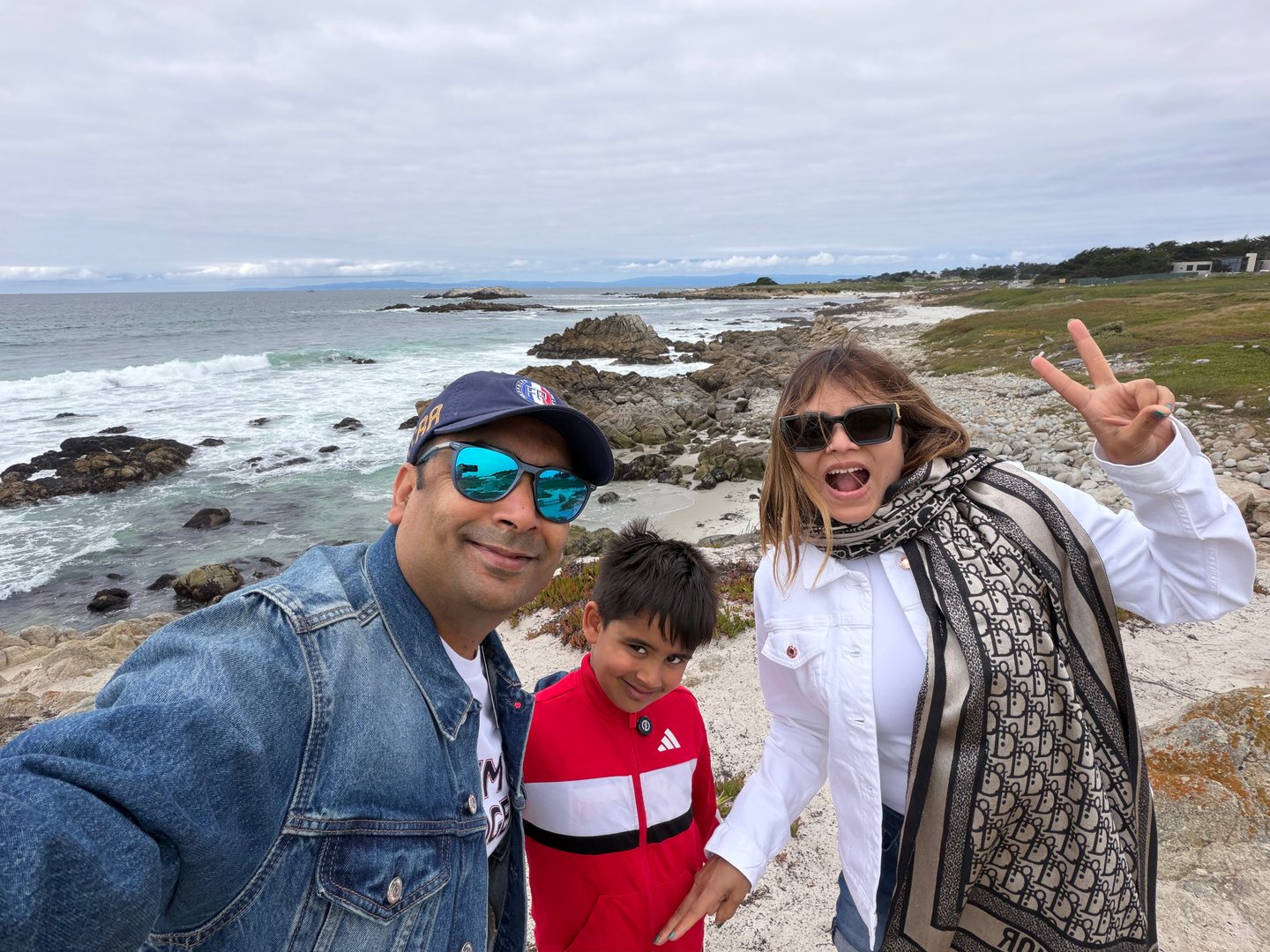 Our family taking a playful selfie beside a rocky coastline with breaking waves.