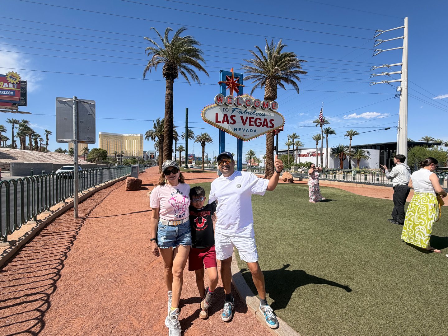 Our family beneath the Welcome to Fabulous Las Vegas Nevada sign, with palm trees and a clear blue sky.